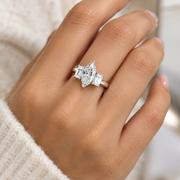 A close-up of a hand wearing a silver ring with a marquise-cut center stone and baguette side stones, set against a soft cream knit sleeve.